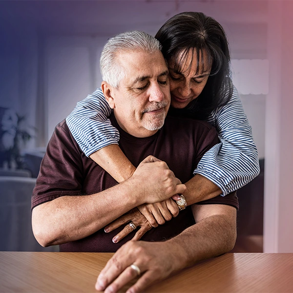 Woman and older man hold hands while she hugs him from behind