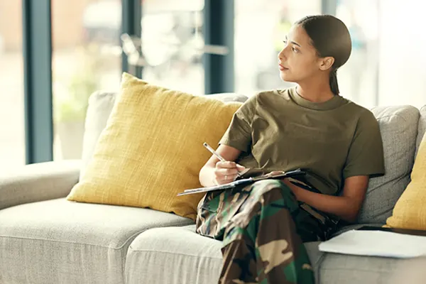Military woman filling out a form while sitting on out a couch
